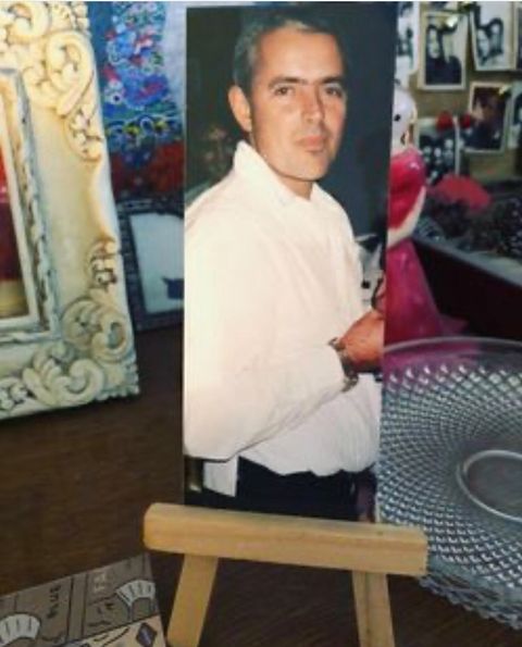 A portrait photo of a man in a white shirt, titled "RECORD" by George Keenen, is displayed on a small wooden easel. Behind it, various decorative items adorn the table.