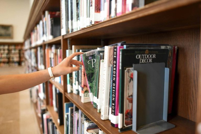 A person reaches for a book on a library shelf filled with various books.