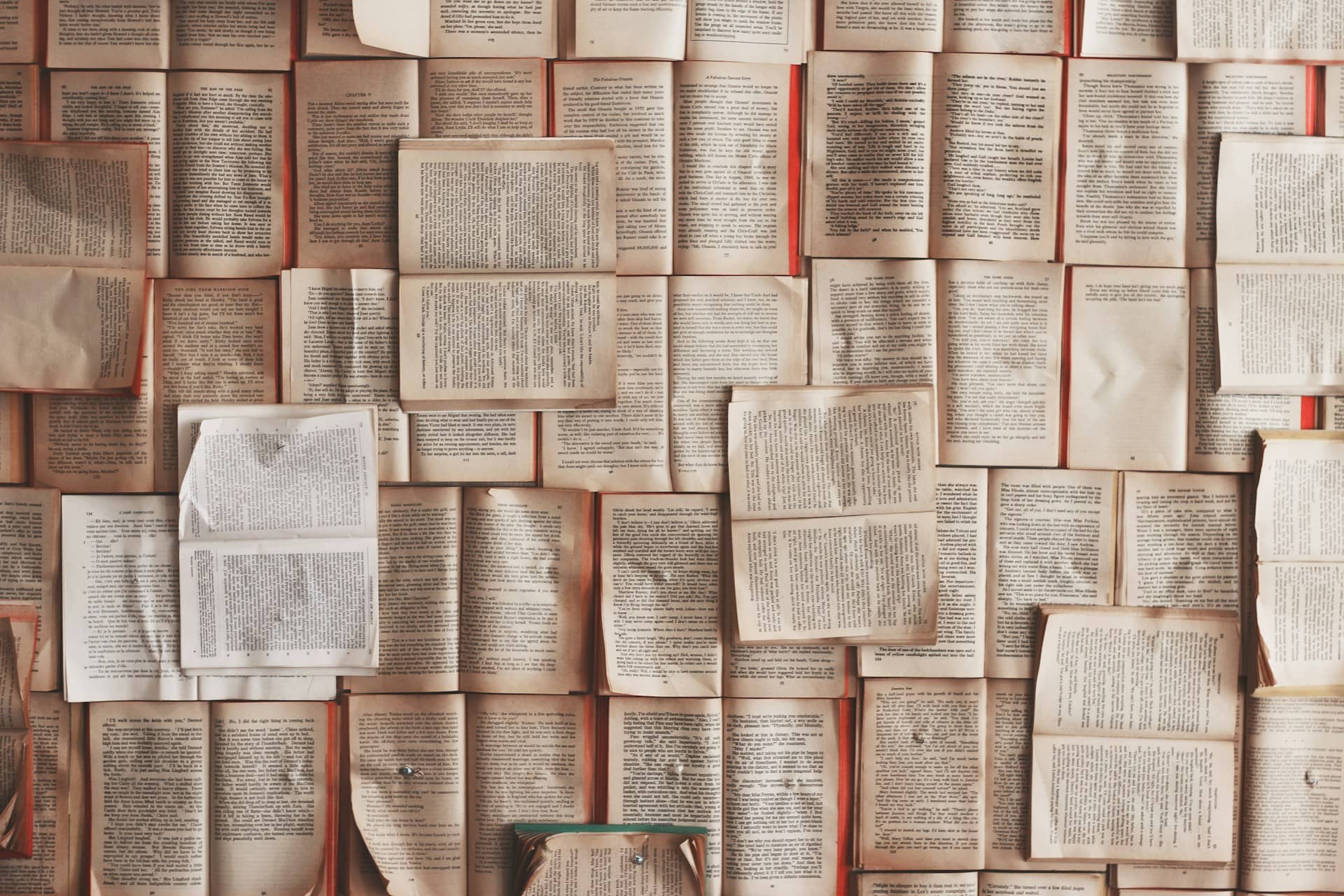 Pages from open books are displayed flat against a wall, creating a layered and overlapping pattern.