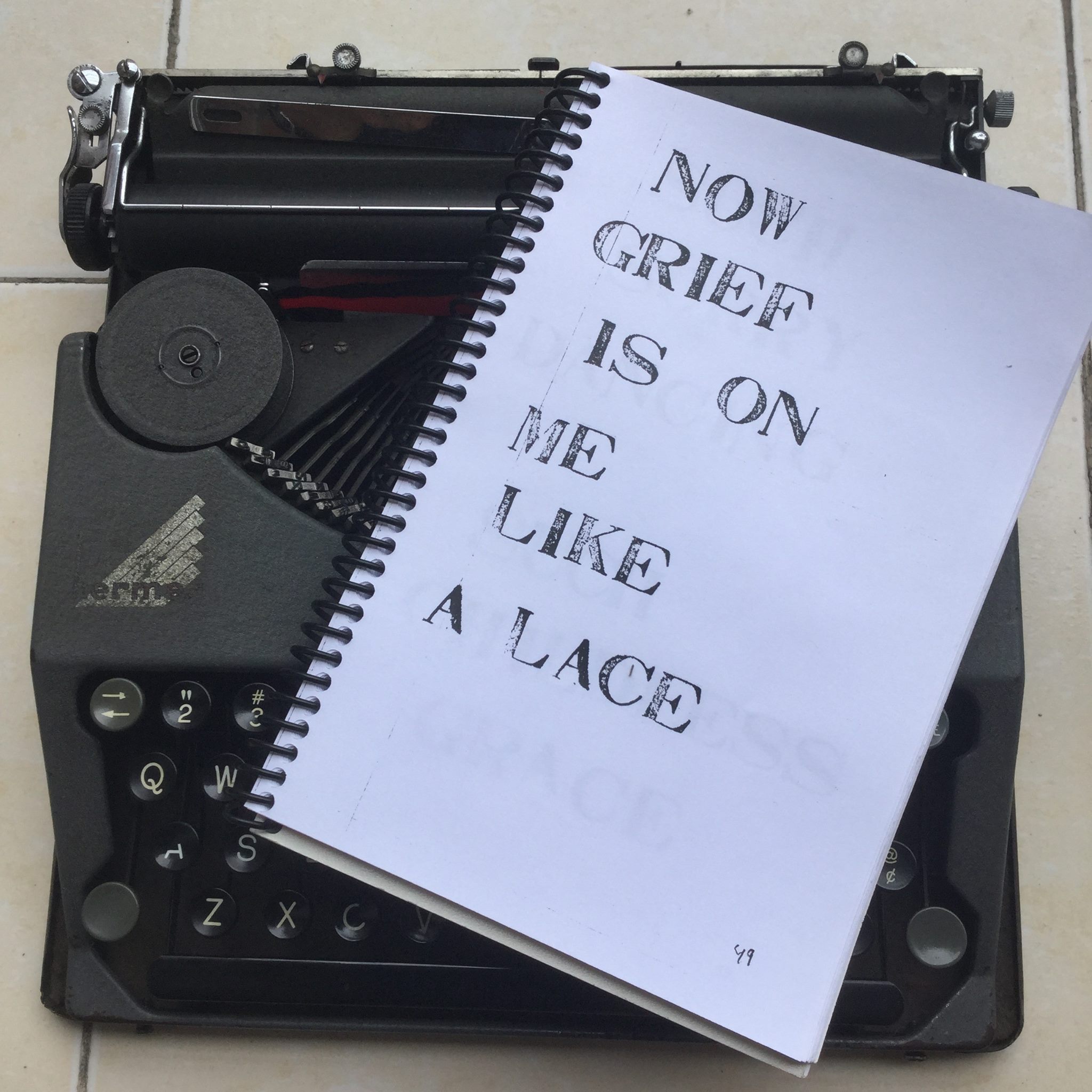 A vintage typewriter with a spiral-bound notebook titled "RECORD, by George Keenen" on it, featuring the text "NOW GRIEF IS ON ME LIKE A LACE" on the cover.