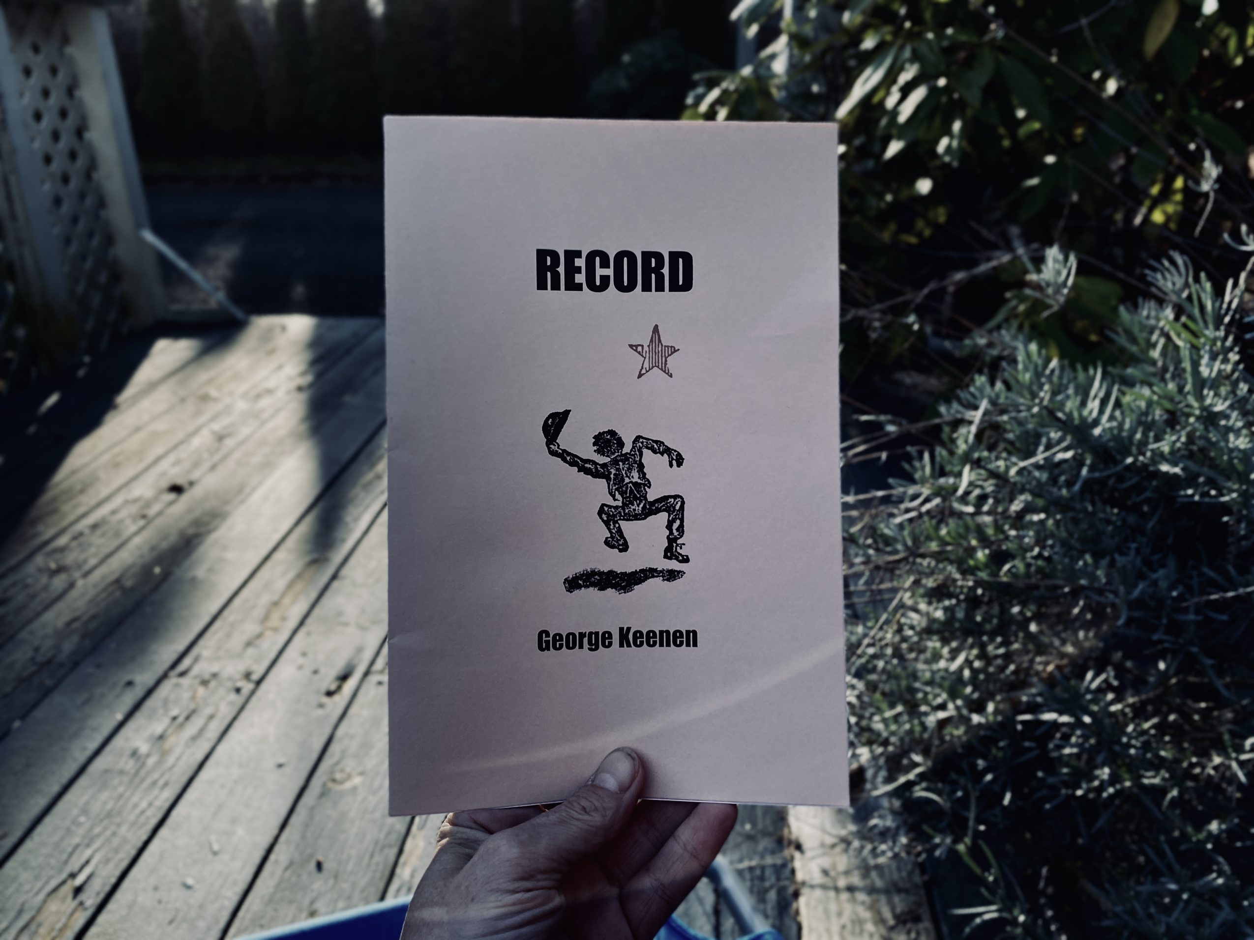 A hand holds a booklet titled "RECORD, by George Keenen," featuring an illustration of a skateboarder on the cover.