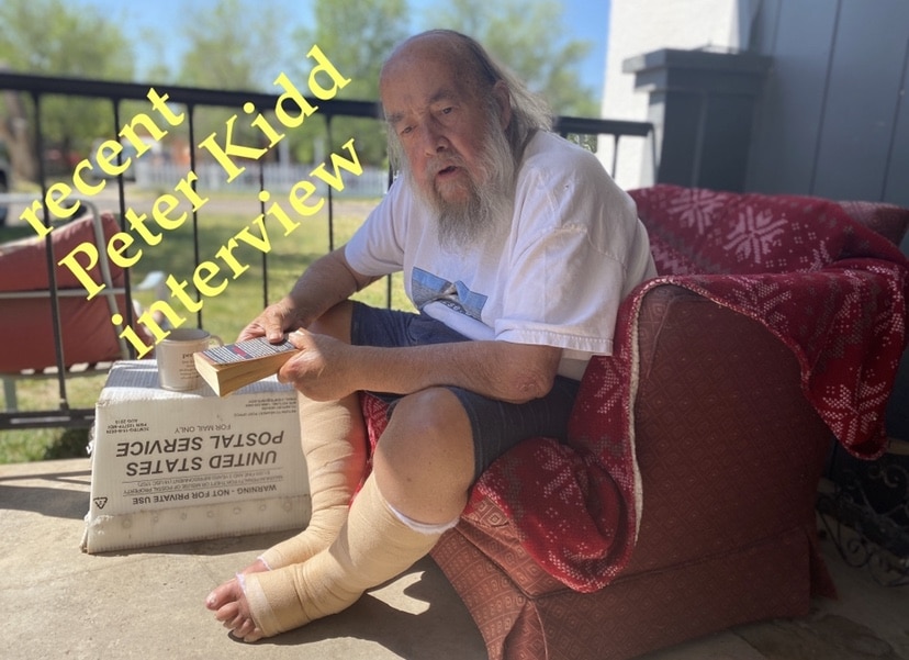 Elderly man with a long beard sits on a porch with a bandaged leg, holding a book. Text reads, "recent Peter Kidd interview.