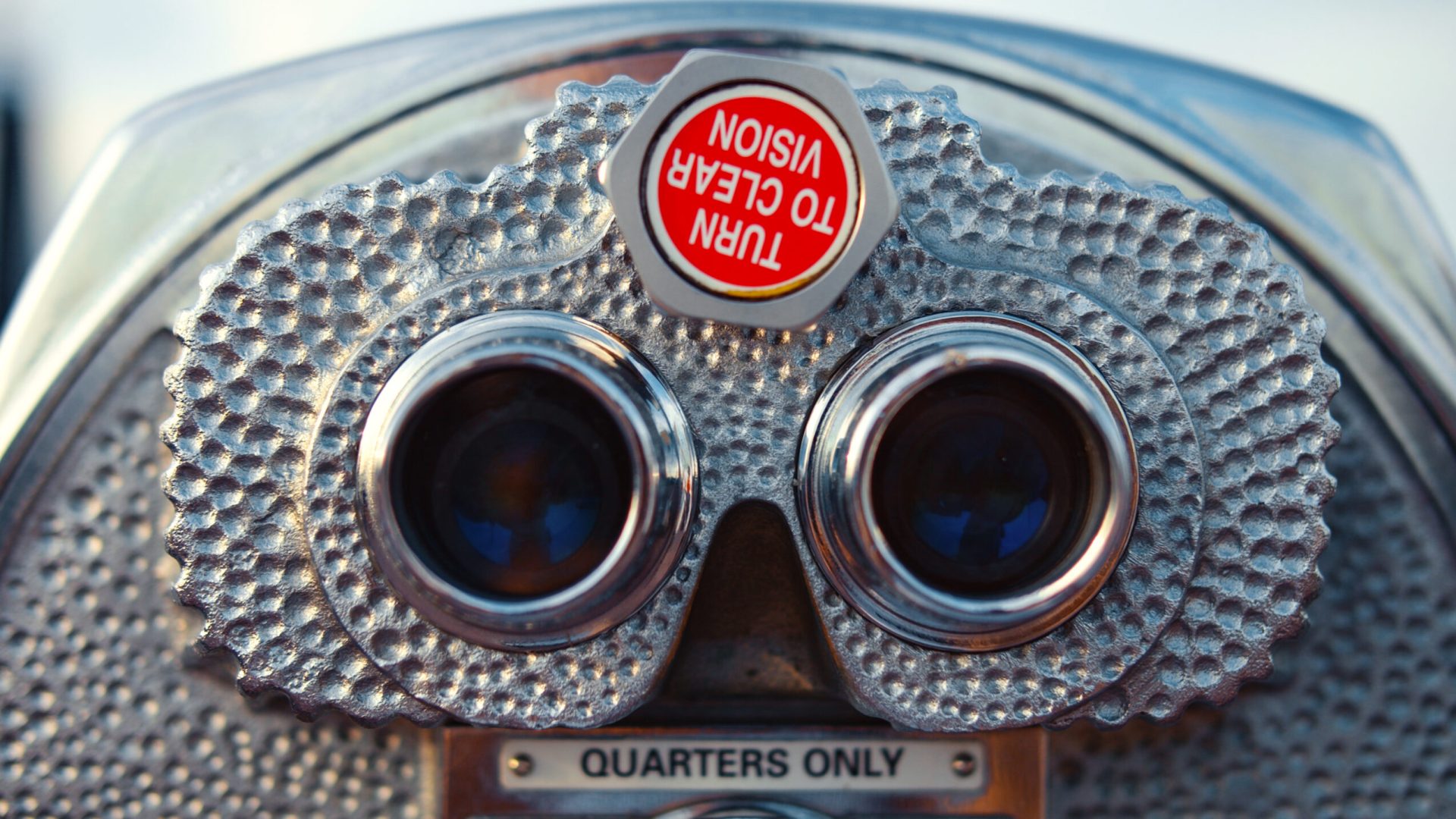 A coin-operated binocular viewer with a textured metal surface and a "Turn to Clear Vision" sign is shown, with a label below reading "Quarters Only.