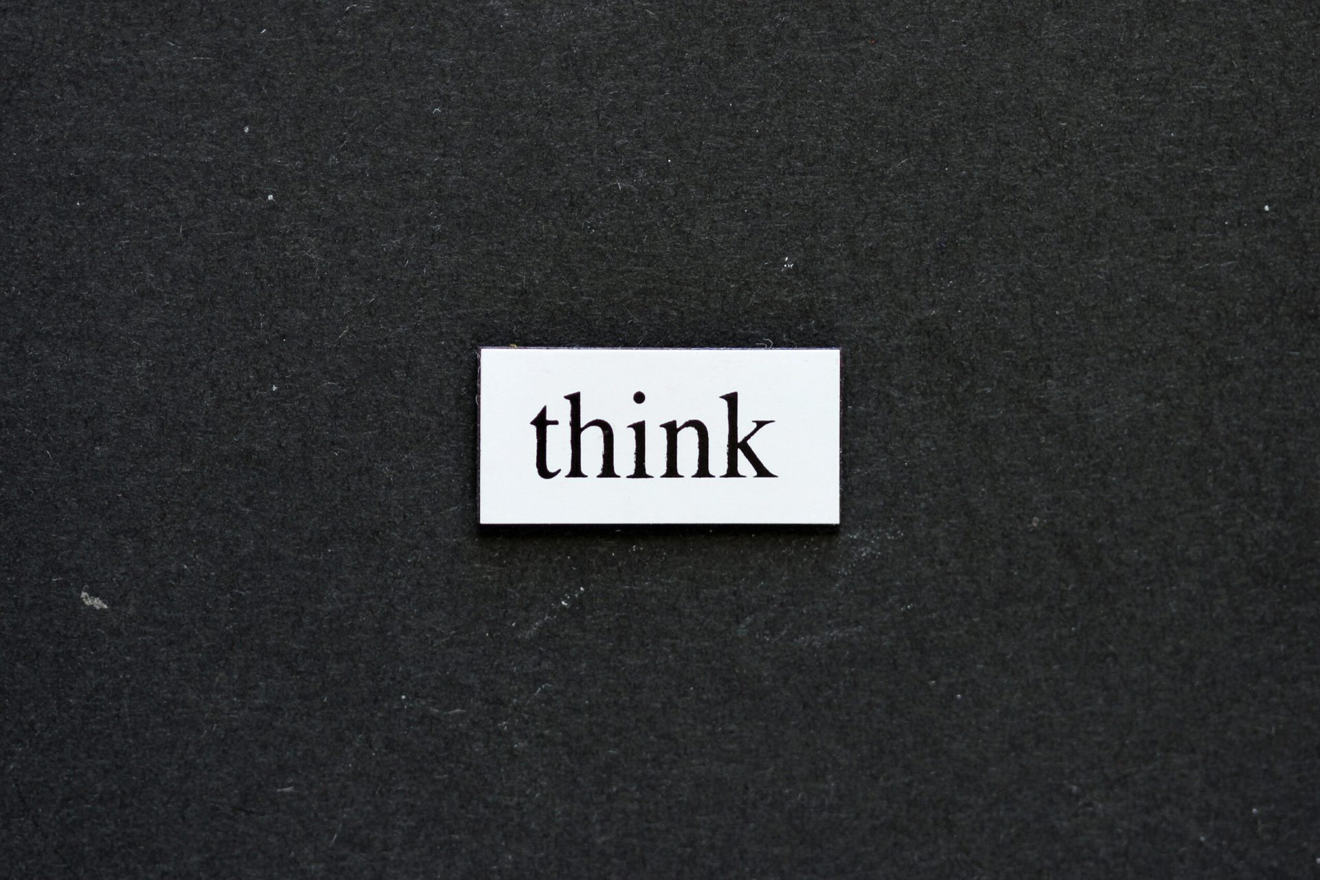 A white rectangular card with the word "think" written in black lowercase letters is placed on a dark gray background.